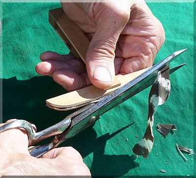 Photo. A man trims a black and white striped feather into arrow fletching using a feather clamp.