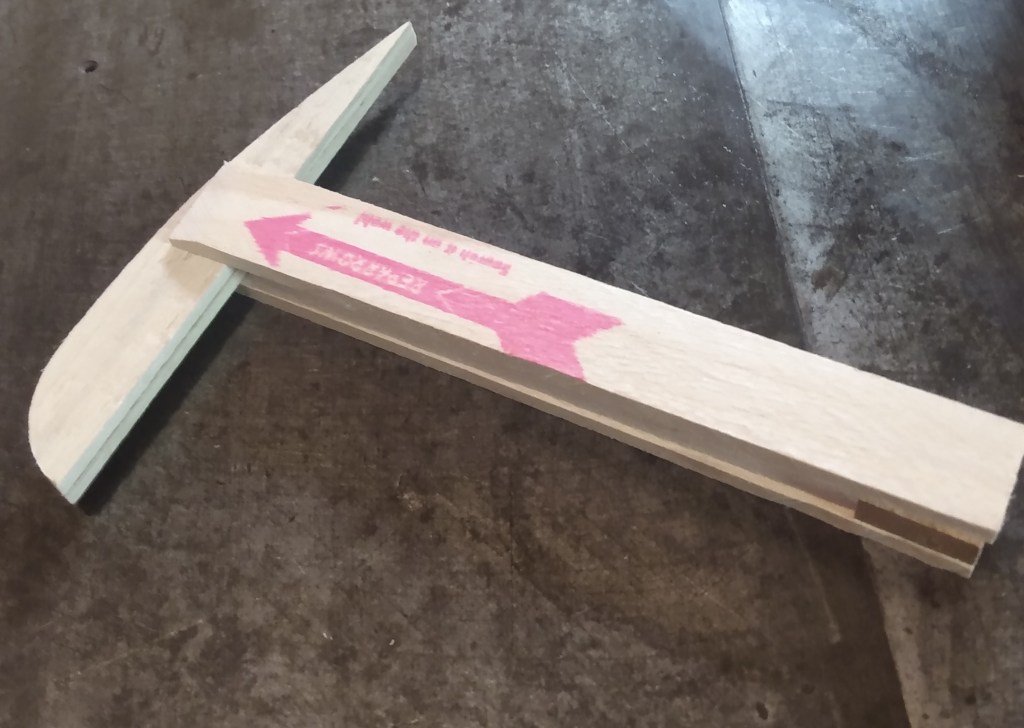 A wooden feather pattern, for trimming fletching feathers, sitting on a leather surface.
